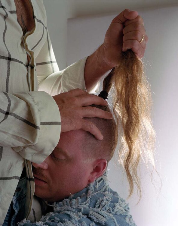 Close-up of a person's face pressed up against another person's torso, with long ponytail pulled upwards