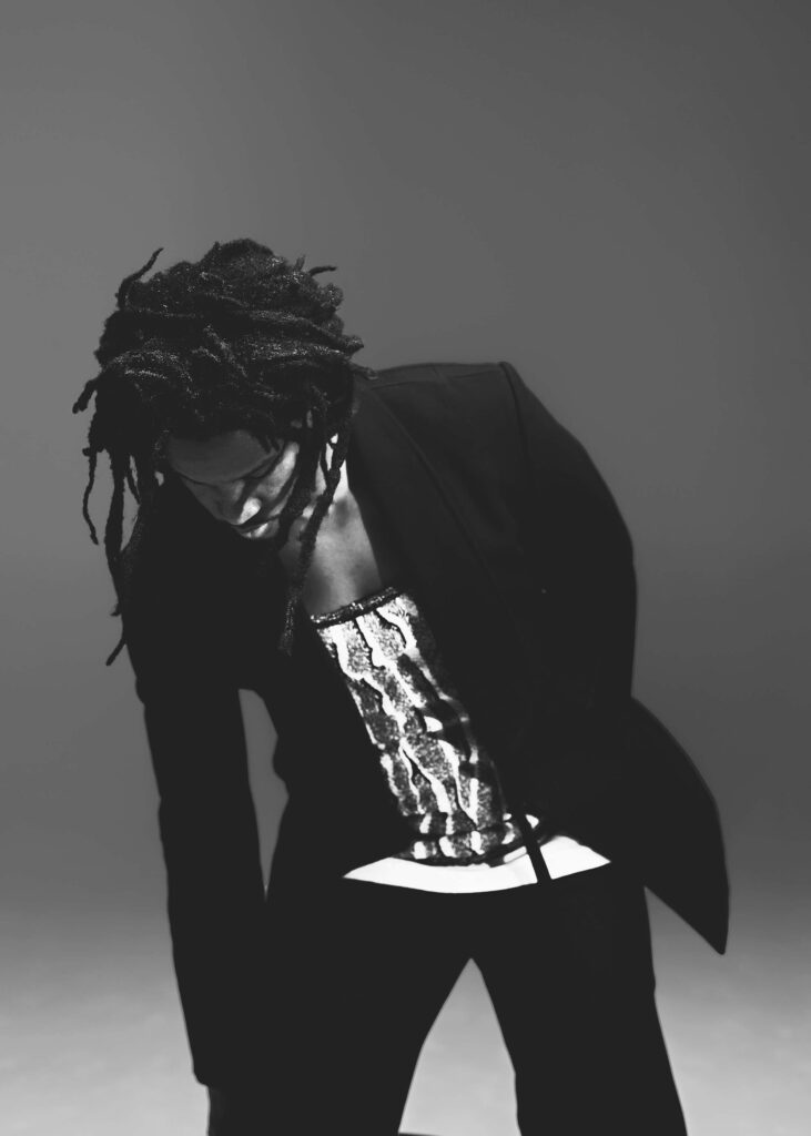 Black and white shot of Akinola reaching down, wearing Bottega tailoring and low-cut top