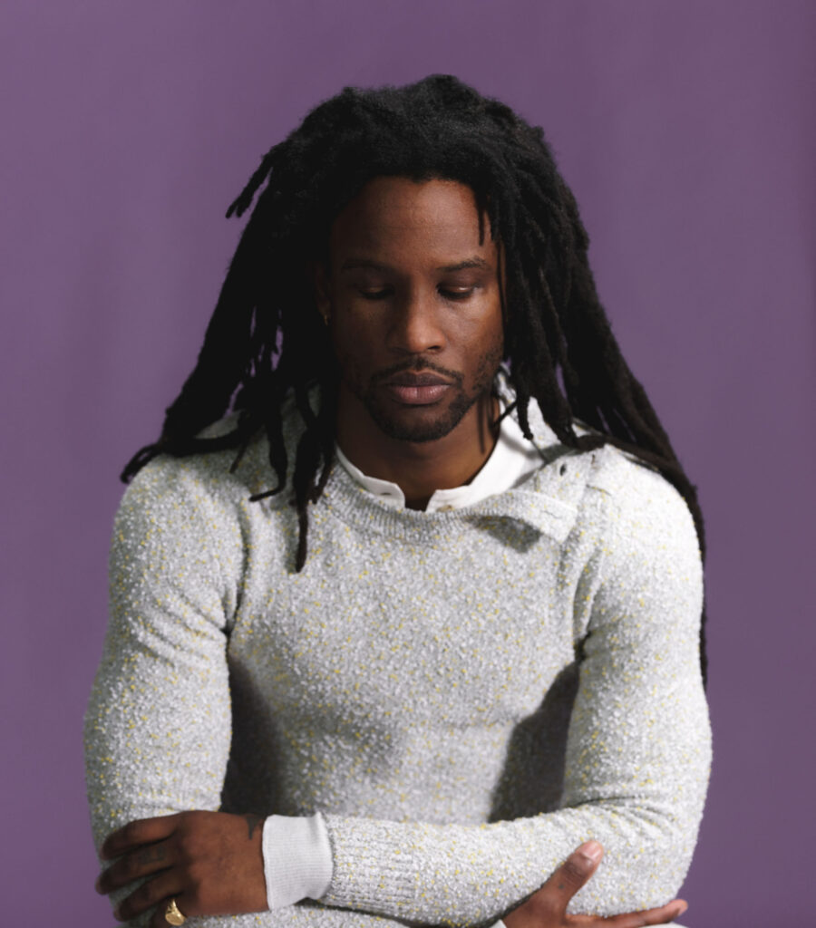 Intimate shot of Akinola against a purple background wearing grey Bottega sweater